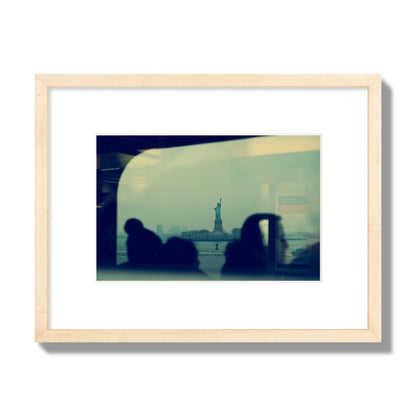 Fine art photograph of passengers silhouetted on a crowded ferry with the Statue of Liberty in the background, archival pigment print, small size, natural wood frame.