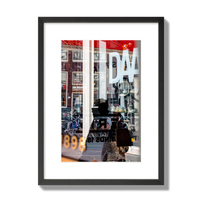 Fine art street photograph of a busy Amsterdam street scene with reflections, silhouettes, shoppers, and store signs. Archival pigment print, medium size, black frame.