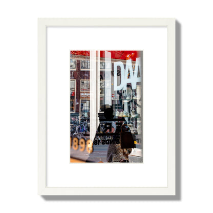 Fine art street photograph of a busy Amsterdam street scene with reflections, silhouettes, shoppers, and store signs. Archival pigment print, small size, white frame.