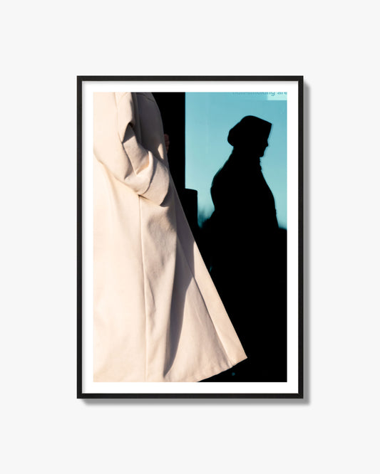 Fine art street photograph of an Amsterdam street scene with a woman's shadow cast against a blue window. Archival pigment print, black frame.