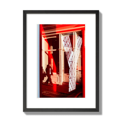 Fine art street photograph of an Amsterdam street scene showing bright red and white reflections of a large letter Y, a man walking, and multiple store fronts. Archival pigment print, medium size, black frame.