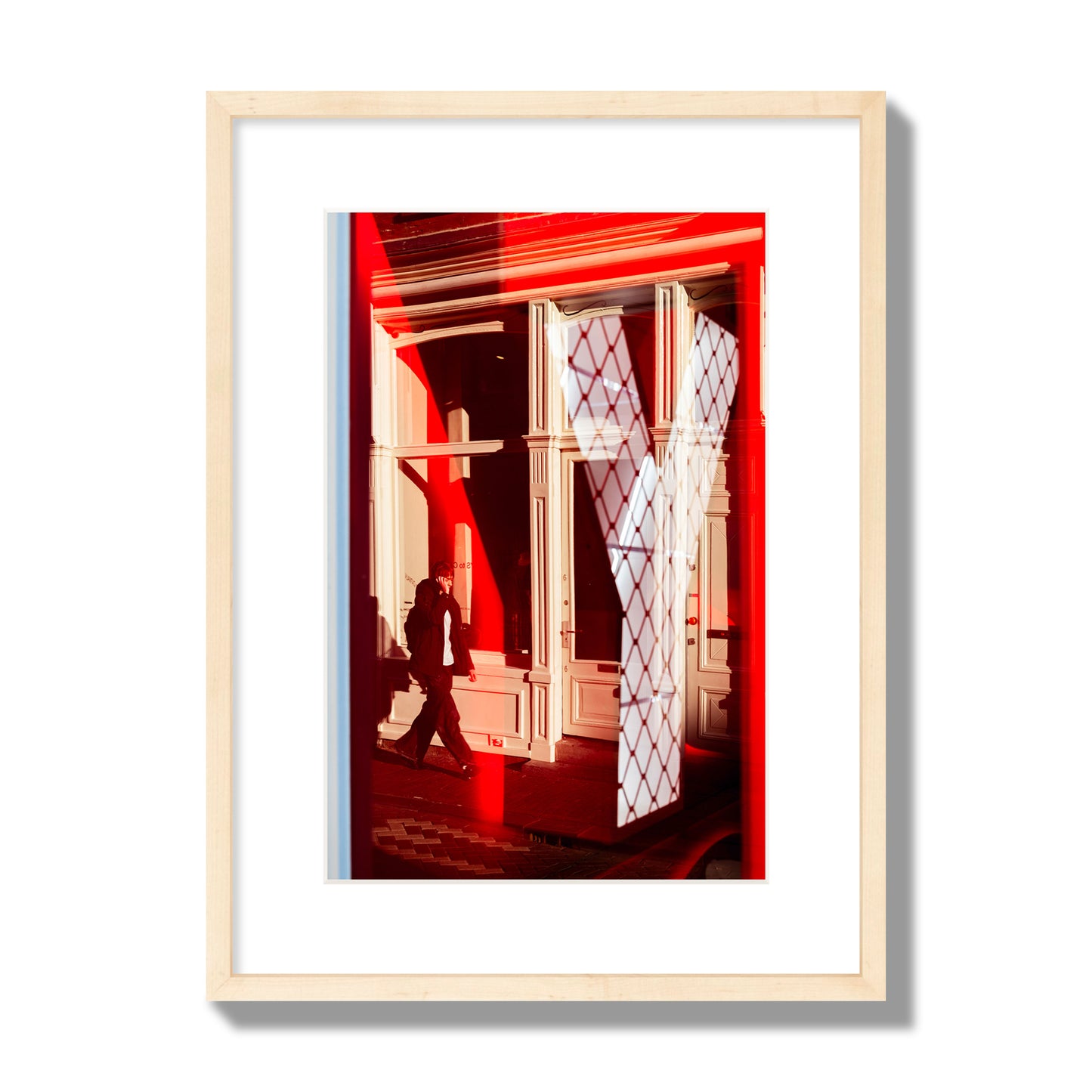 Fine art street photograph of an Amsterdam street scene showing bright red and white reflections of a large letter Y, a man walking, and multiple store fronts. Archival pigment print, medium size, natural wood frame.