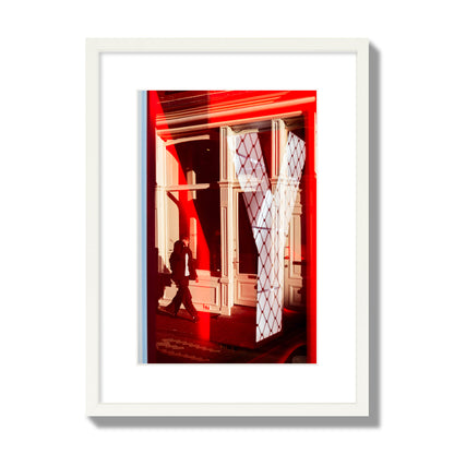 Fine art street photograph of an Amsterdam street scene showing bright red and white reflections of a large letter Y, a man walking, and multiple store fronts. Archival pigment print, medium size, white frame.