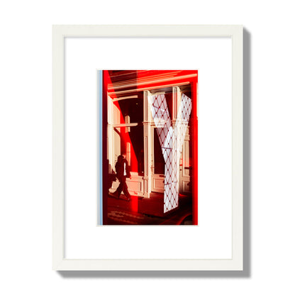 Fine art street photograph of an Amsterdam street scene showing bright red and white reflections of a large letter Y, a man walking, and multiple store fronts. Archival pigment print, small size, white frame.