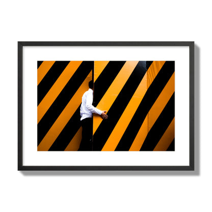 Fine art street photograph of a man opening an orange and black stripped construction door. Archival pigment print, large size, black frame.