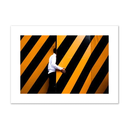 Fine art street photograph of a man opening an orange and black stripped construction door. Archival pigment print, large size, unframed.