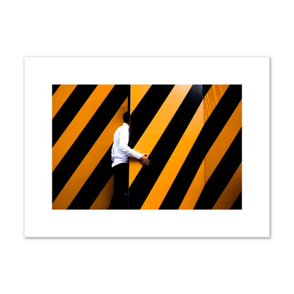 Fine art street photograph of a man opening an orange and black stripped construction door. Archival pigment print, medium size, unframed.