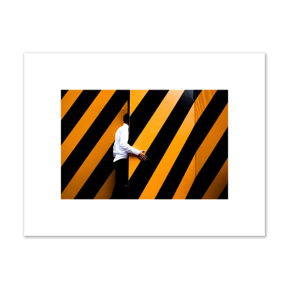 Fine art street photograph of a man opening an orange and black stripped construction door. Archival pigment print, small size, unframed.