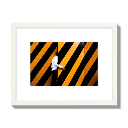 Fine art street photograph of a man opening an orange and black stripped construction door. Archival pigment print, small size, white frame.