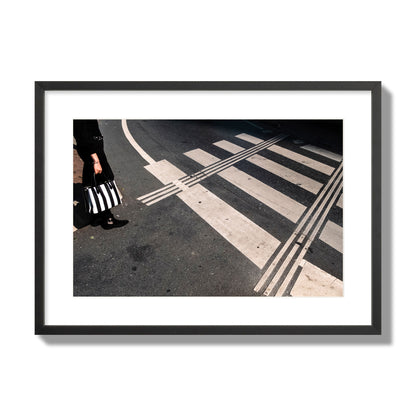 Fine art street photograph of a woman holding a black and white striped purse while crossing a black and white crosswalk. Archival pigment print, large size, black frame.