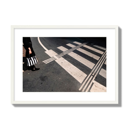Fine art street photograph of a woman holding a black and white striped purse while crossing a black and white crosswalk. Archival pigment print, large size, white frame.