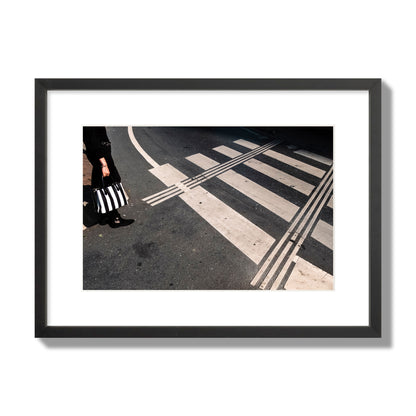 Fine art street photograph of a woman holding a black and white striped purse while crossing a black and white crosswalk. Archival pigment print, medium size, black frame.