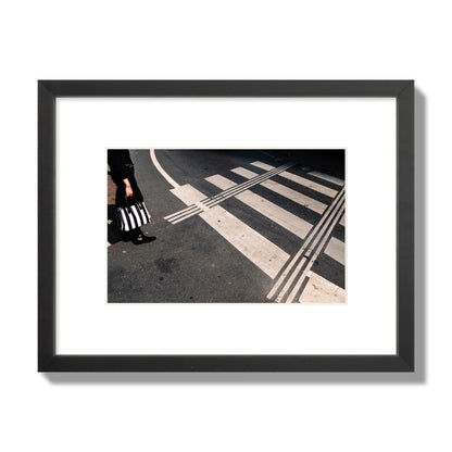 Fine art street photograph of a woman holding a black and white striped purse while crossing a black and white crosswalk. Archival pigment print, small size, black frame.