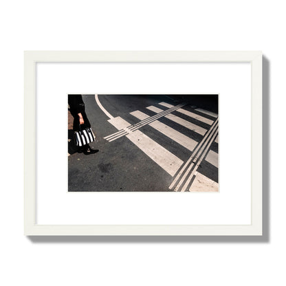 Fine art street photograph of a woman holding a black and white striped purse while crossing a black and white crosswalk. Archival pigment print, small size, white frame.