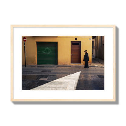 Fine art street photograph of an elderly man walking down a Valencia, Spain street with yellow and green walls, illuminated by a shaft of light. Archival pigment print, large size, natural wood frame.