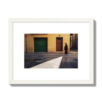 Fine art street photograph of an elderly man walking down a Valencia, Spain street with yellow and green walls, illuminated by a shaft of light. Archival pigment print, small size, white frame.