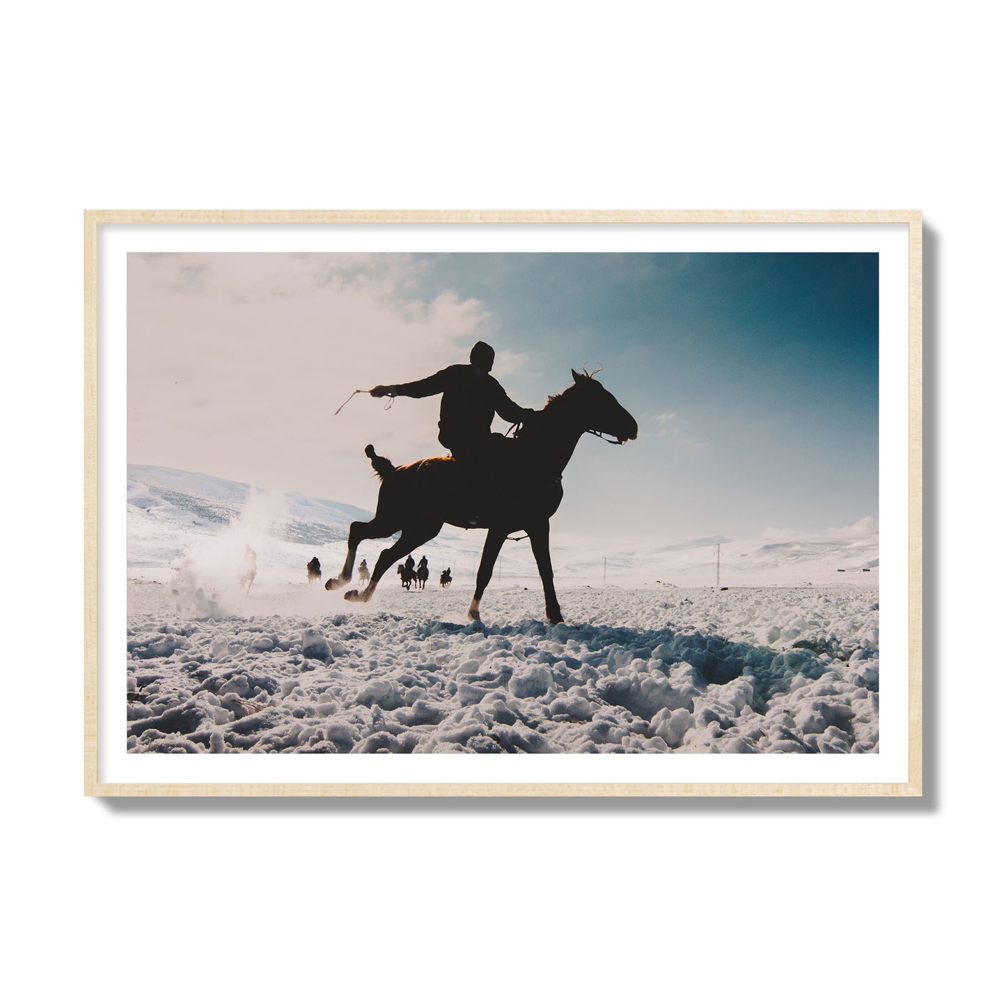 Fine art photography of a silhouetted man riding a galloping horse in a snowy field with a mountain backdrop, archival pigment print, collector size, natural wood frame.