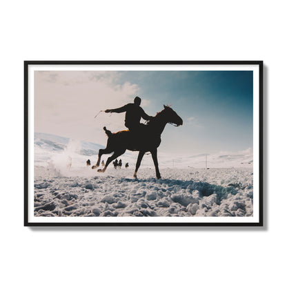 Fine art photography of a silhouetted man riding a galloping horse in a snowy field with a mountain backdrop, archival pigment print, gallery size, black frame.