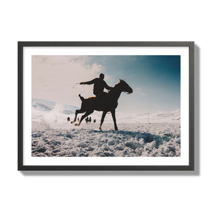 Fine art photography of a silhouetted man riding a galloping horse in a snowy field with a mountain backdrop, archival pigment print, giant size, black frame.