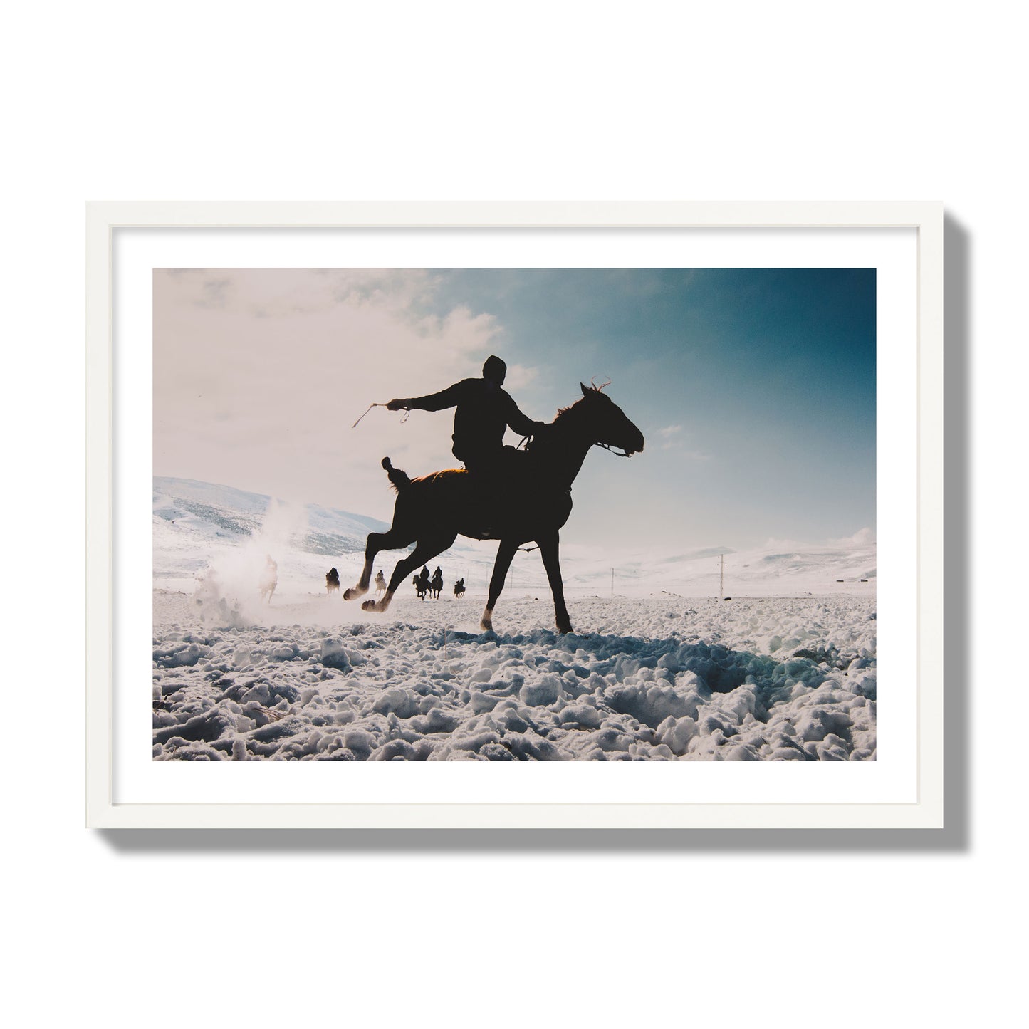 Fine art photography of a silhouetted man riding a galloping horse in a snowy field with a mountain backdrop, archival pigment print, giant size, white frame.