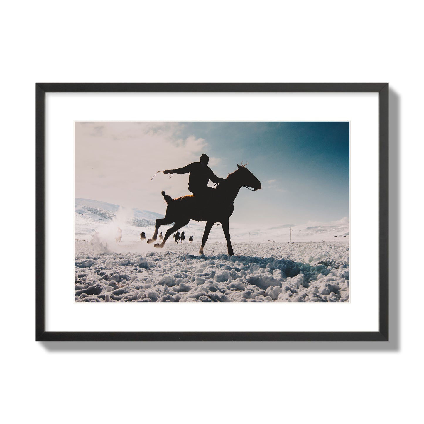 Fine art photography of a silhouetted man riding a galloping horse in a snowy field with a mountain backdrop, archival pigment print, large size, black frame.