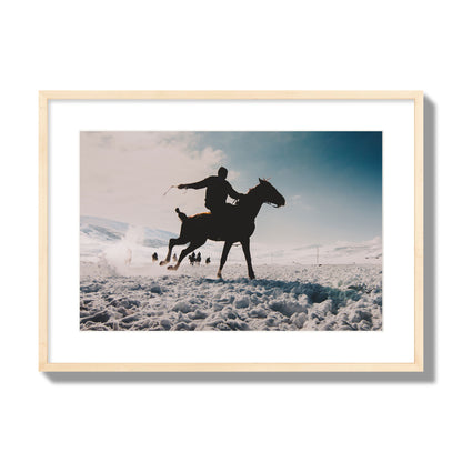 Fine art photography of a silhouetted man riding a galloping horse in a snowy field with a mountain backdrop, archival pigment print, large size, natural wood frame.