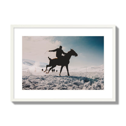 Fine art photography of a silhouetted man riding a galloping horse in a snowy field with a mountain backdrop, archival pigment print, large size, white frame.