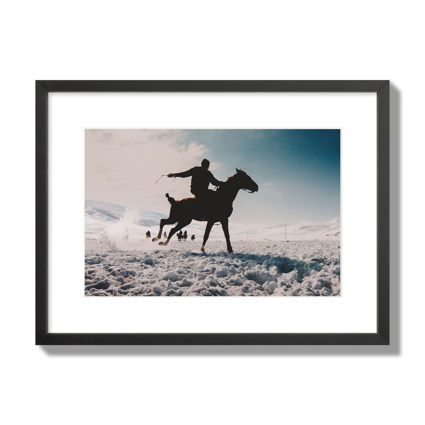 Fine art photography of a silhouetted man riding a galloping horse in a snowy field with a mountain backdrop, archival pigment print, medium size, black frame.
