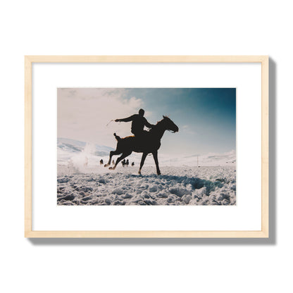Fine art photography of a silhouetted man riding a galloping horse in a snowy field with a mountain backdrop, archival pigment print, medium size, natural wood frame.