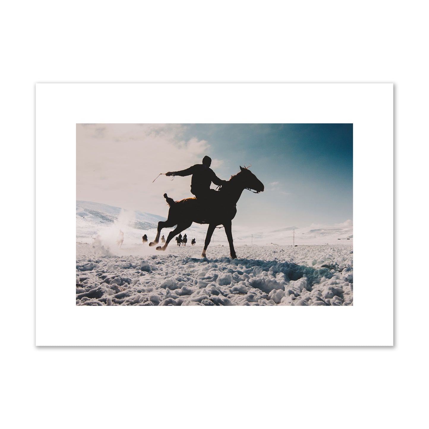 Fine art photography of a silhouetted man riding a galloping horse in a snowy field with a mountain backdrop, archival pigment print, medium size, print.