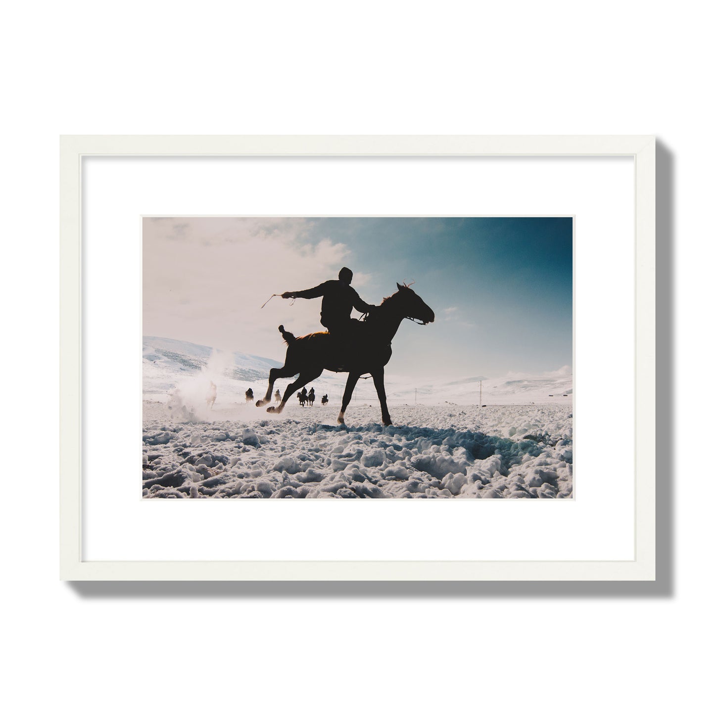 Fine art photography of a silhouetted man riding a galloping horse in a snowy field with a mountain backdrop, archival pigment print, medium size, white frame.