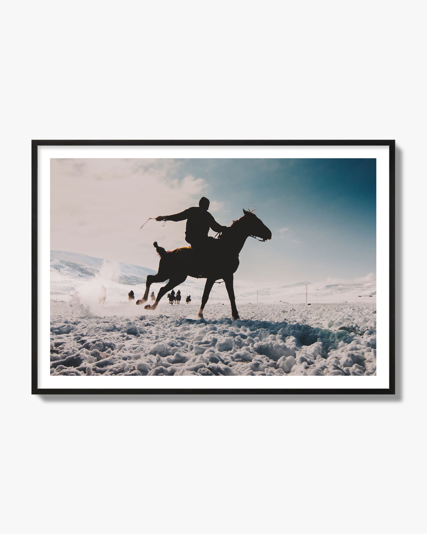 Fine art photography of a silhouetted man riding a galloping horse in a snowy field with a mountain backdrop, archival pigment print, black frame.
