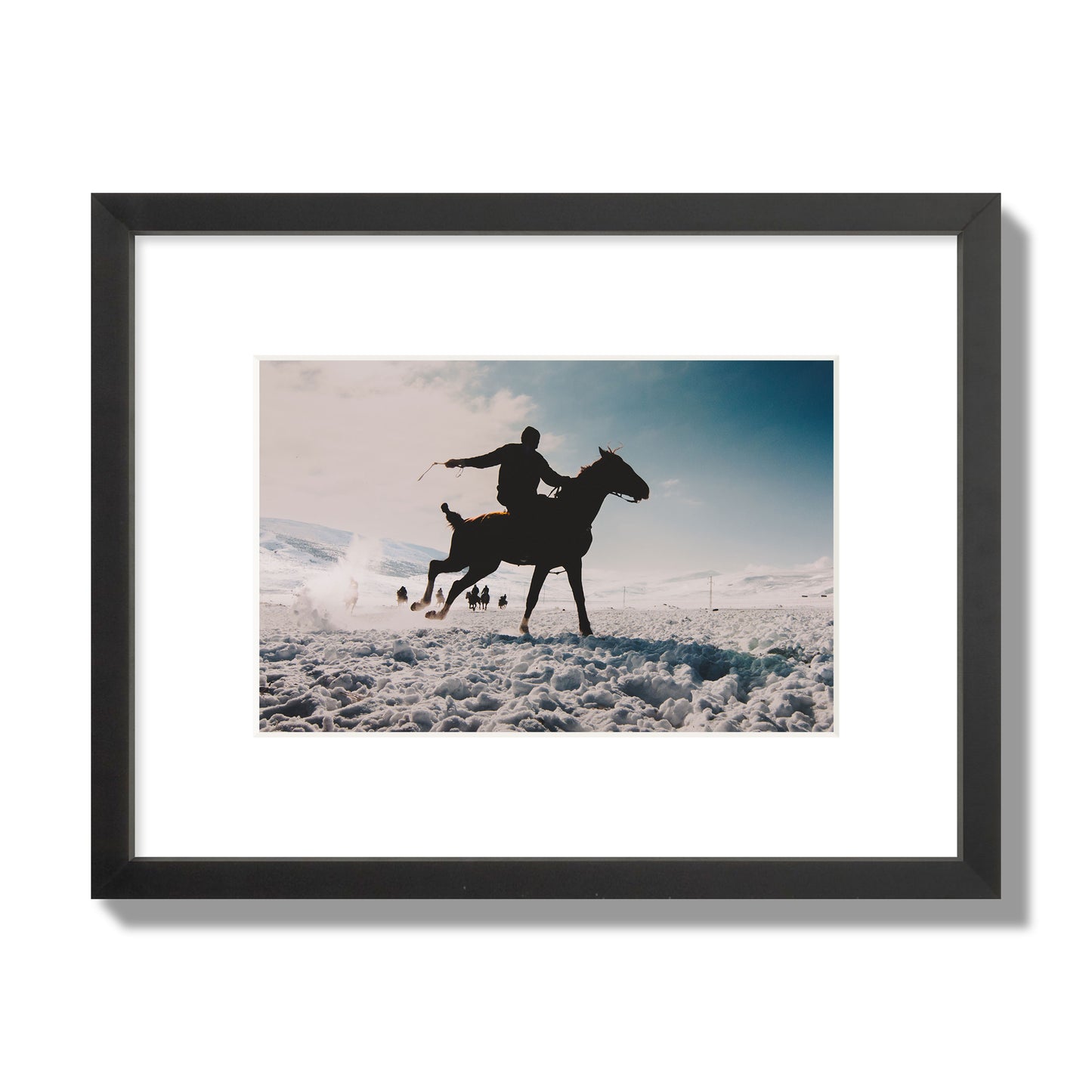 Fine art photography of a silhouetted man riding a galloping horse in a snowy field with a mountain backdrop, archival pigment print, small size, black frame.