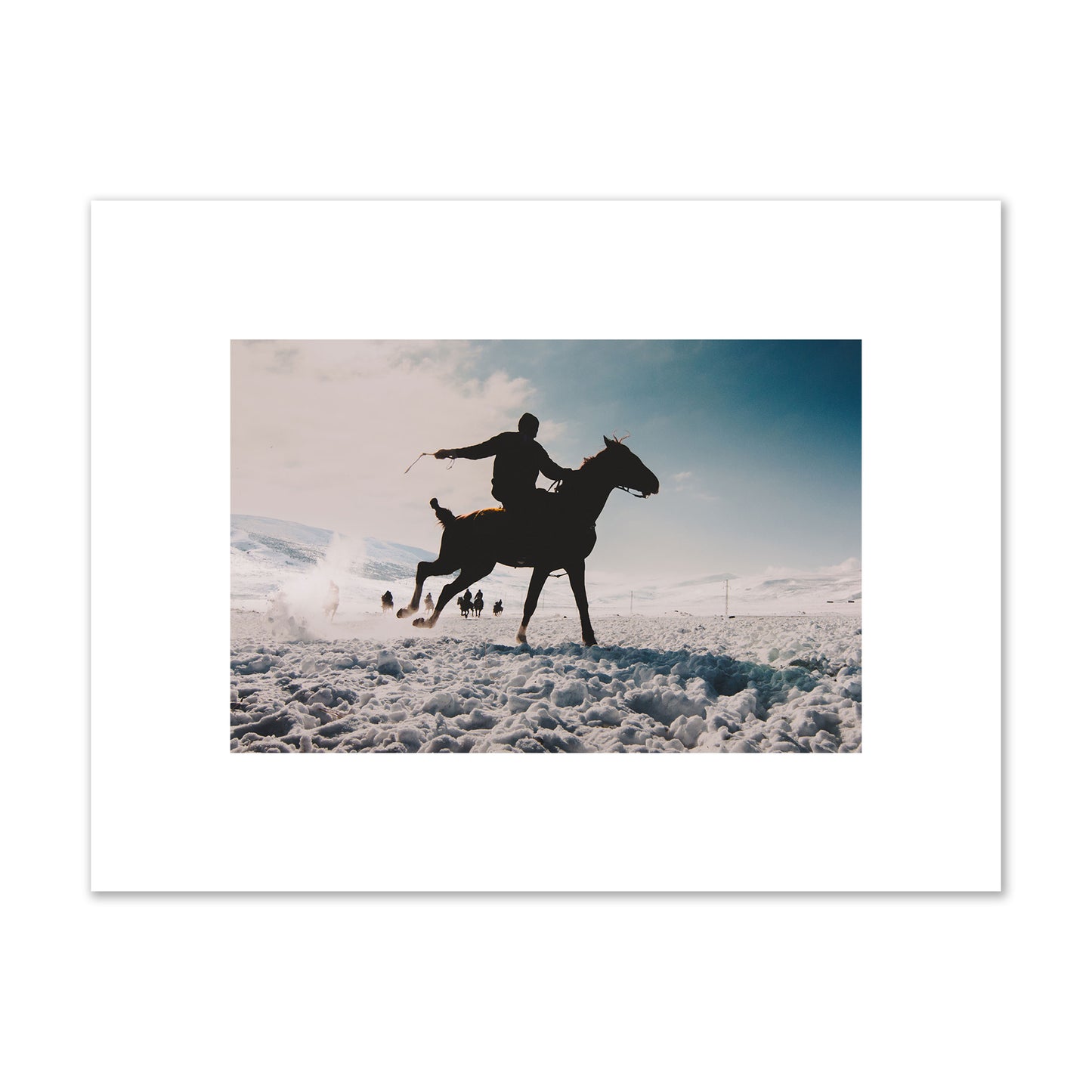 Fine art photography of a silhouetted man riding a galloping horse in a snowy field with a mountain backdrop, archival pigment print, small size, print.