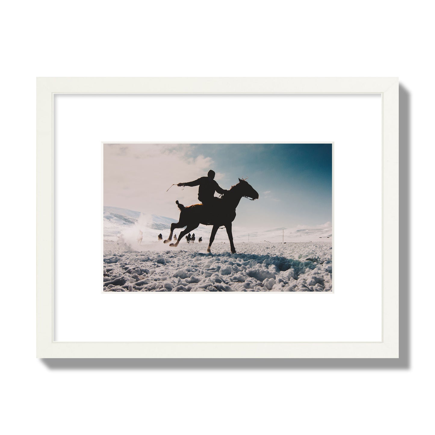 Fine art photography of a silhouetted man riding a galloping horse in a snowy field with a mountain backdrop, archival pigment print, small size, white frame.