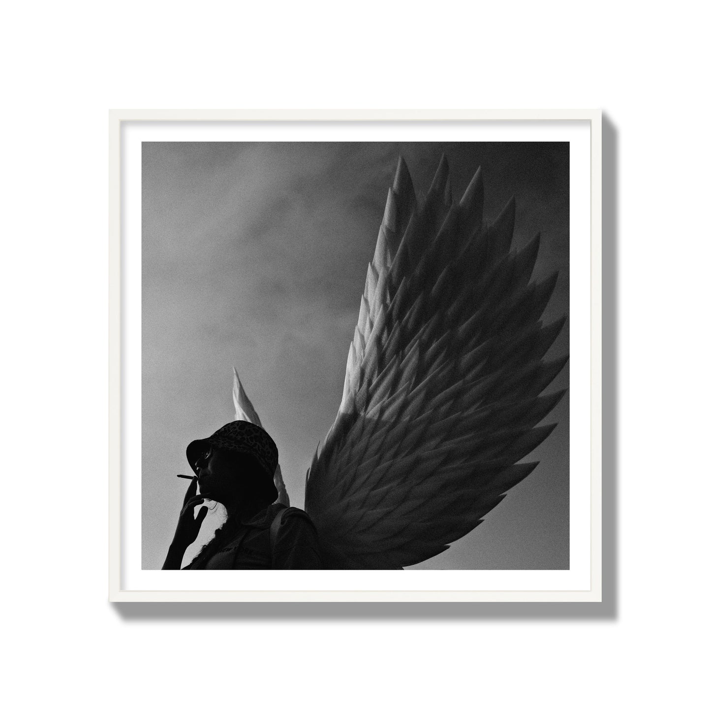 Fine art photography of a woman smoking in front of a winged statue, archival pigment print, gallery size, white frame.