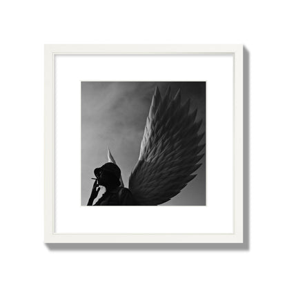 Fine art photography of a woman smoking in front of a winged statue, archival pigment print, medium size, white frame.