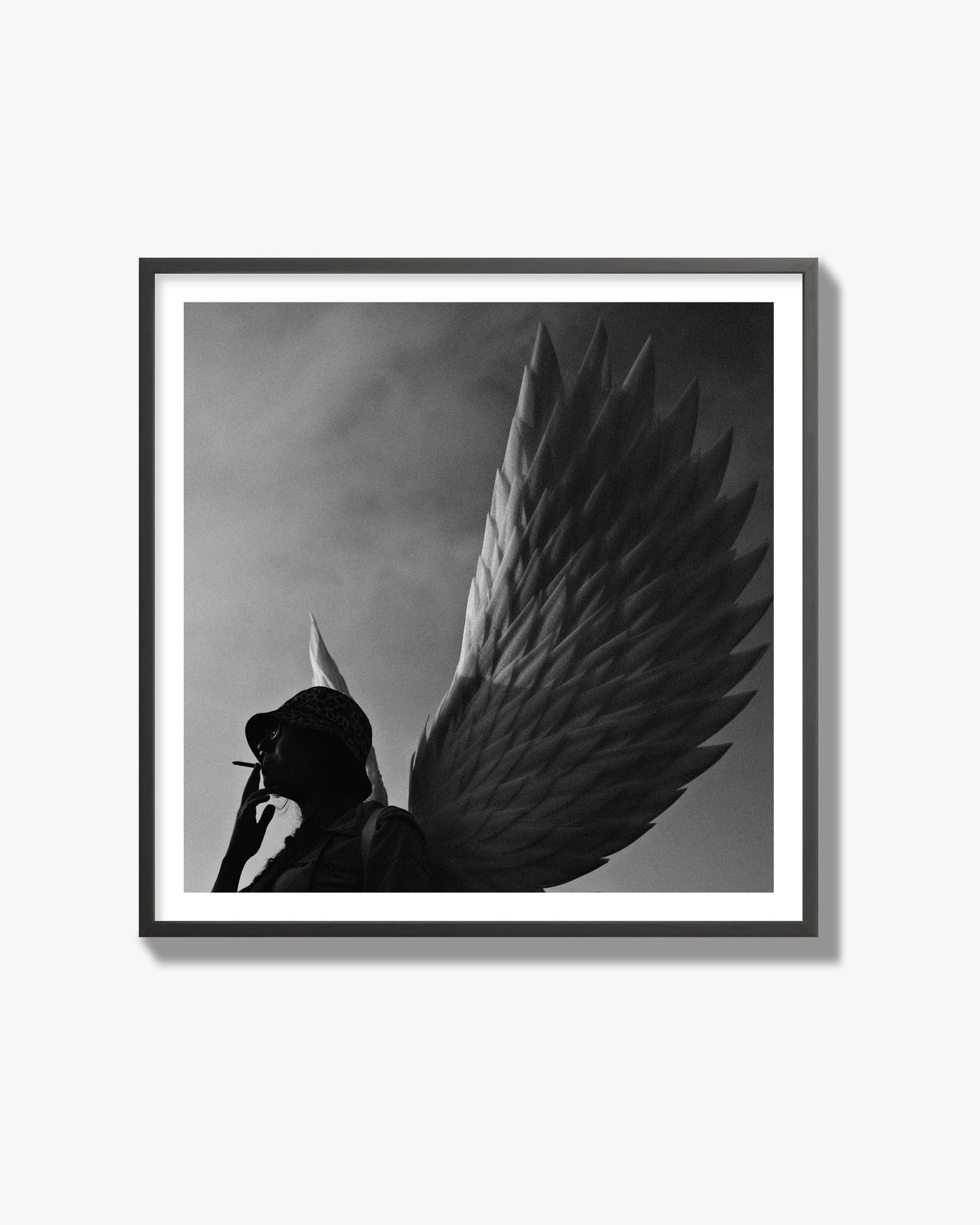 Fine art photography of a woman smoking in front of a winged statue, archival pigment print, black frame.