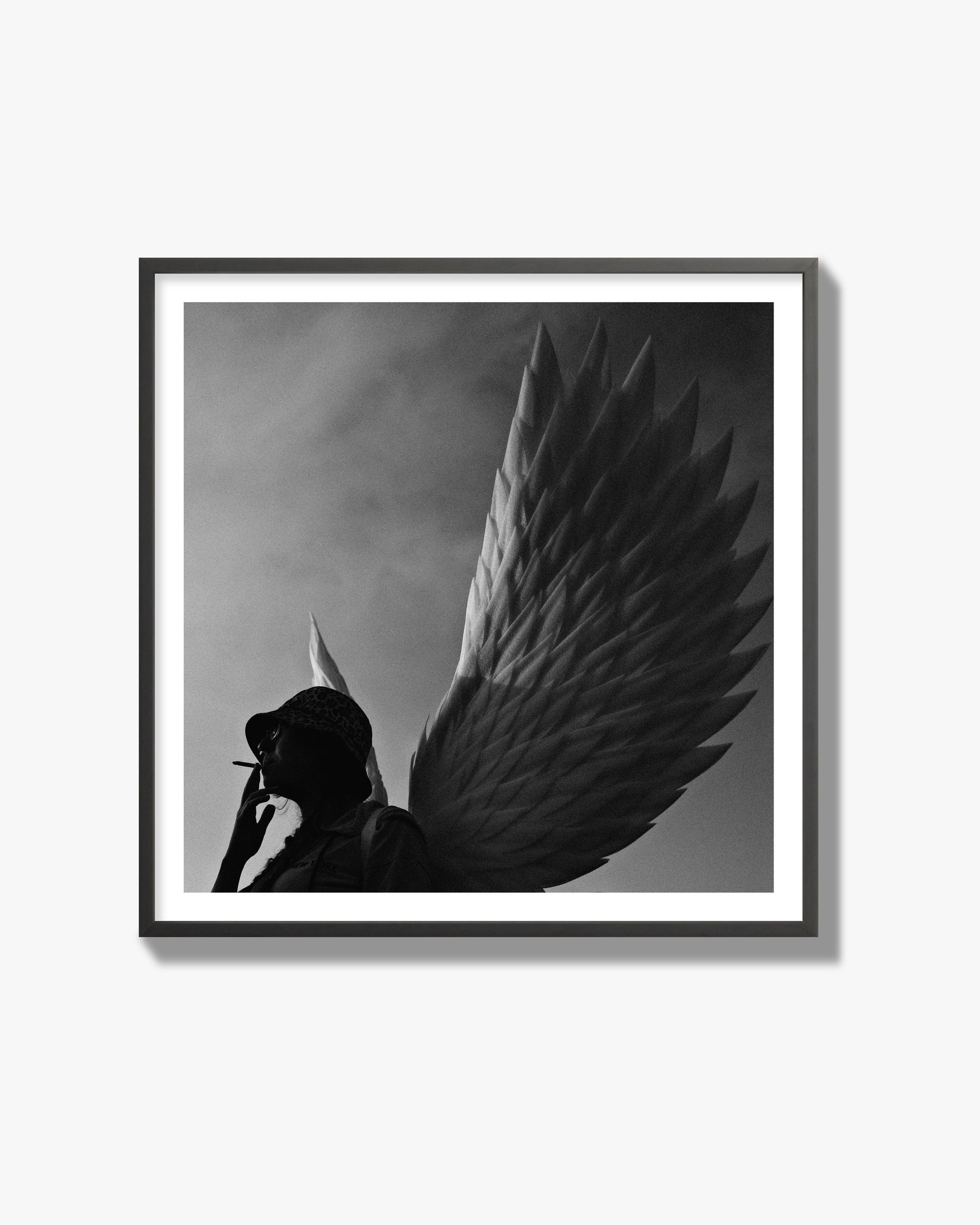 Fine art photography of a woman smoking in front of a winged statue, archival pigment print, black frame.