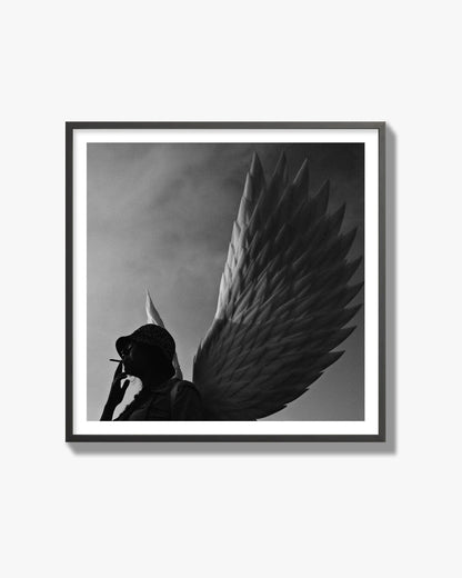 Fine art photography of a woman smoking in front of a winged statue, archival pigment print, black frame.