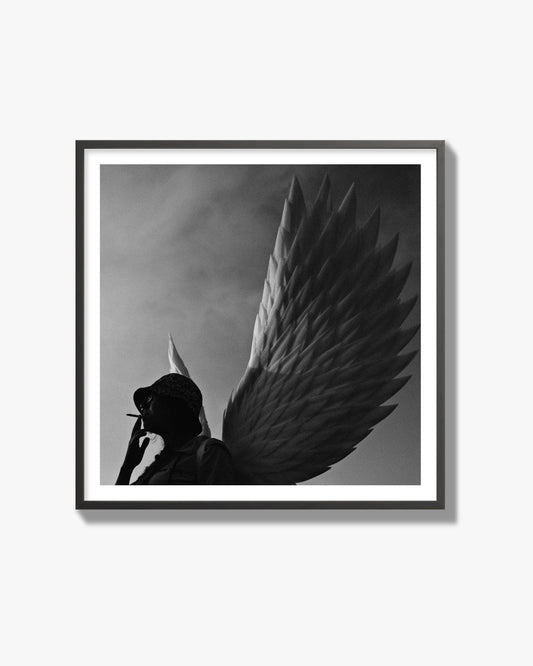 Fine art photography of a woman smoking in front of a winged statue, archival pigment print, black frame.